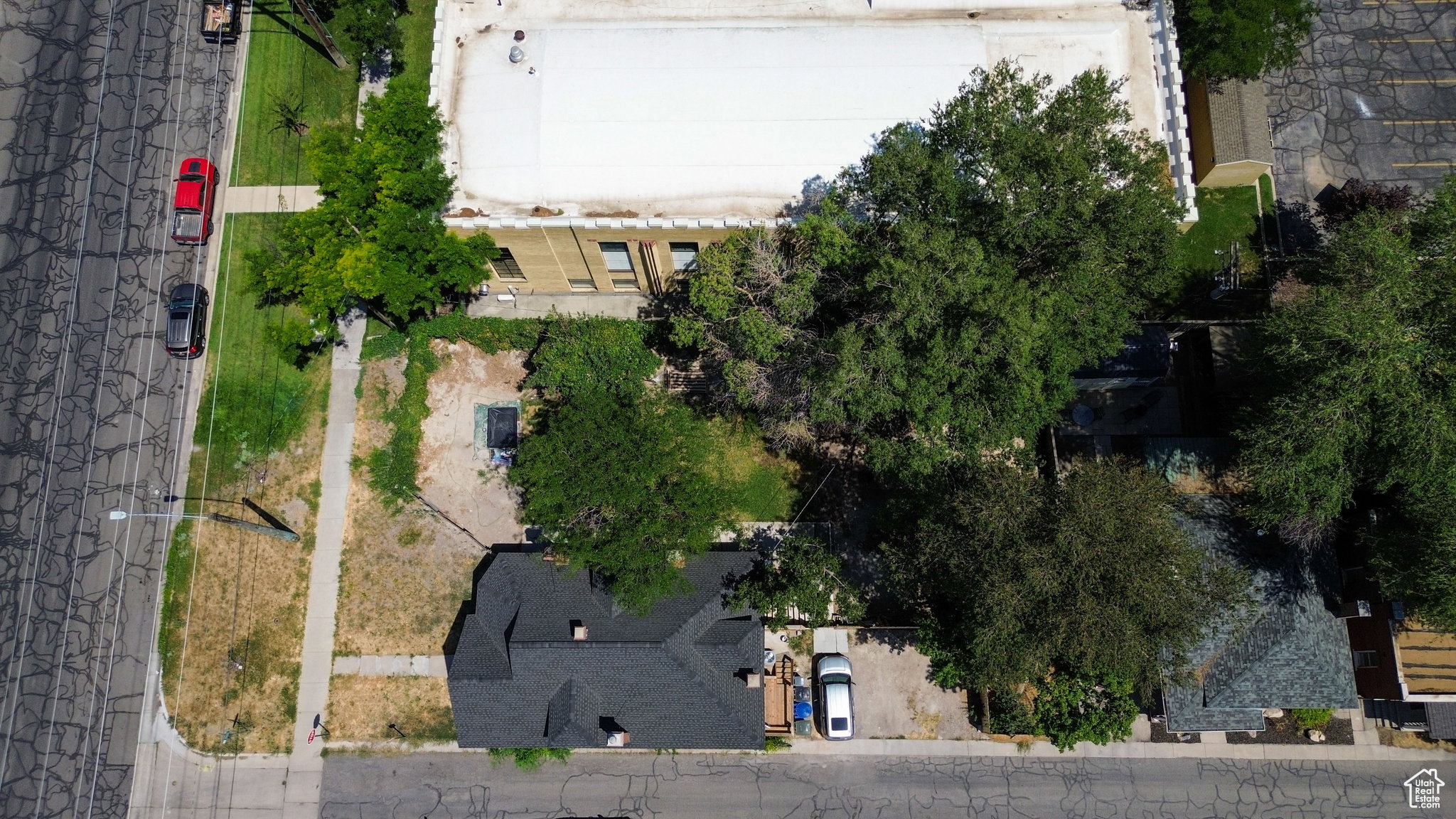 Corner property with a dark shingled roof, mature trees, and a paved driveway
