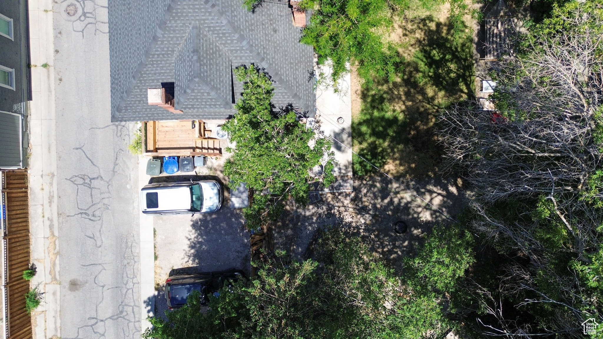 Shingle roof with chimney, wood deck, concrete driveway, and mature trees