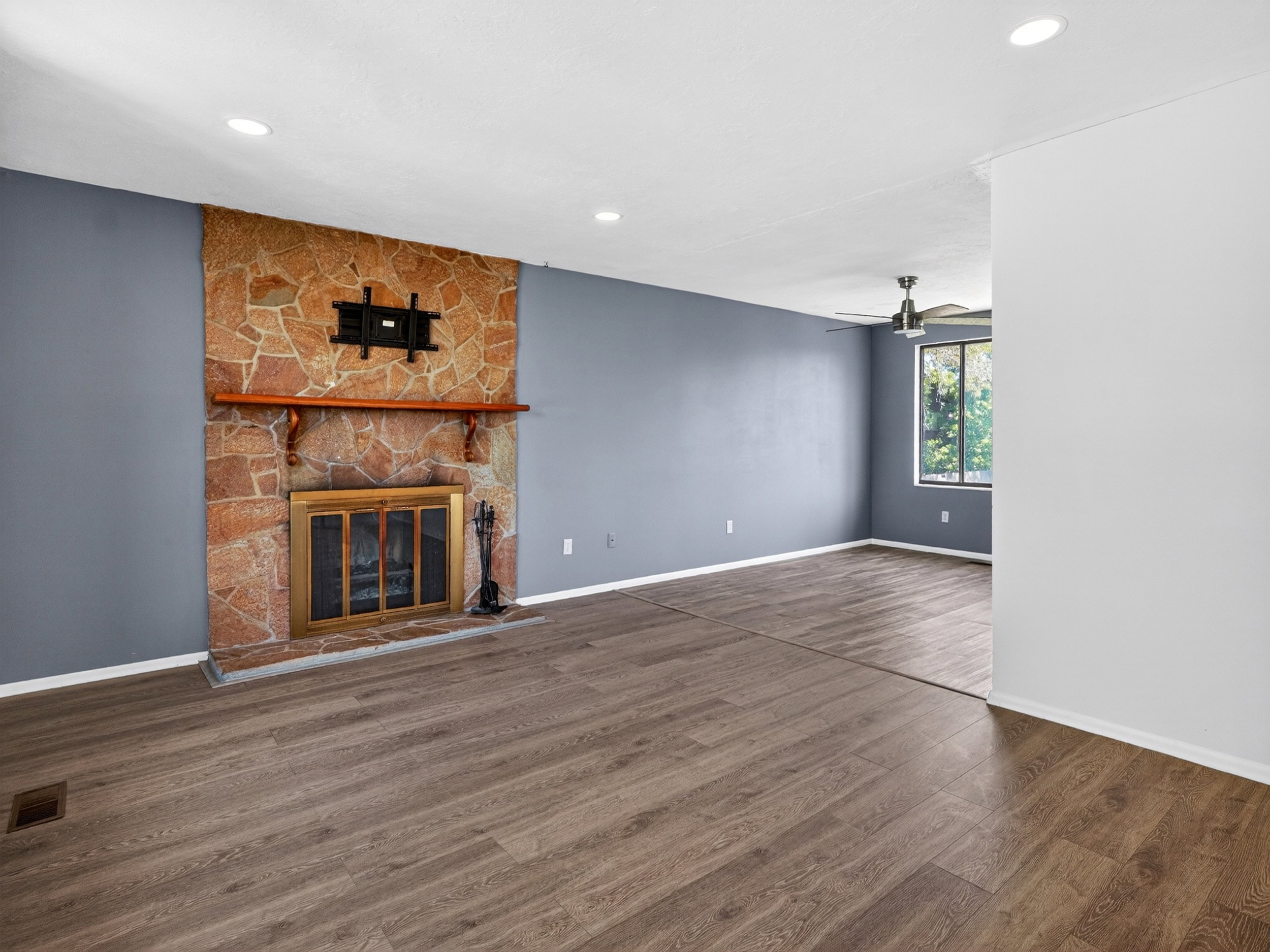 Living area featuring a stone-clad fireplace with a wood mantel, wood-finish flooring, recessed lighting, and a ceiling fan