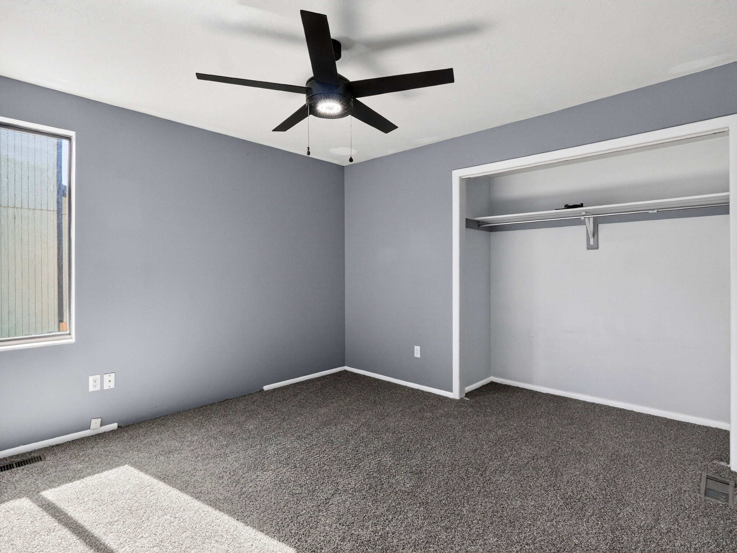 Room featuring gray wall paint, gray carpeting, a window with white trim, and a built-in closet with shelving and hanging rod