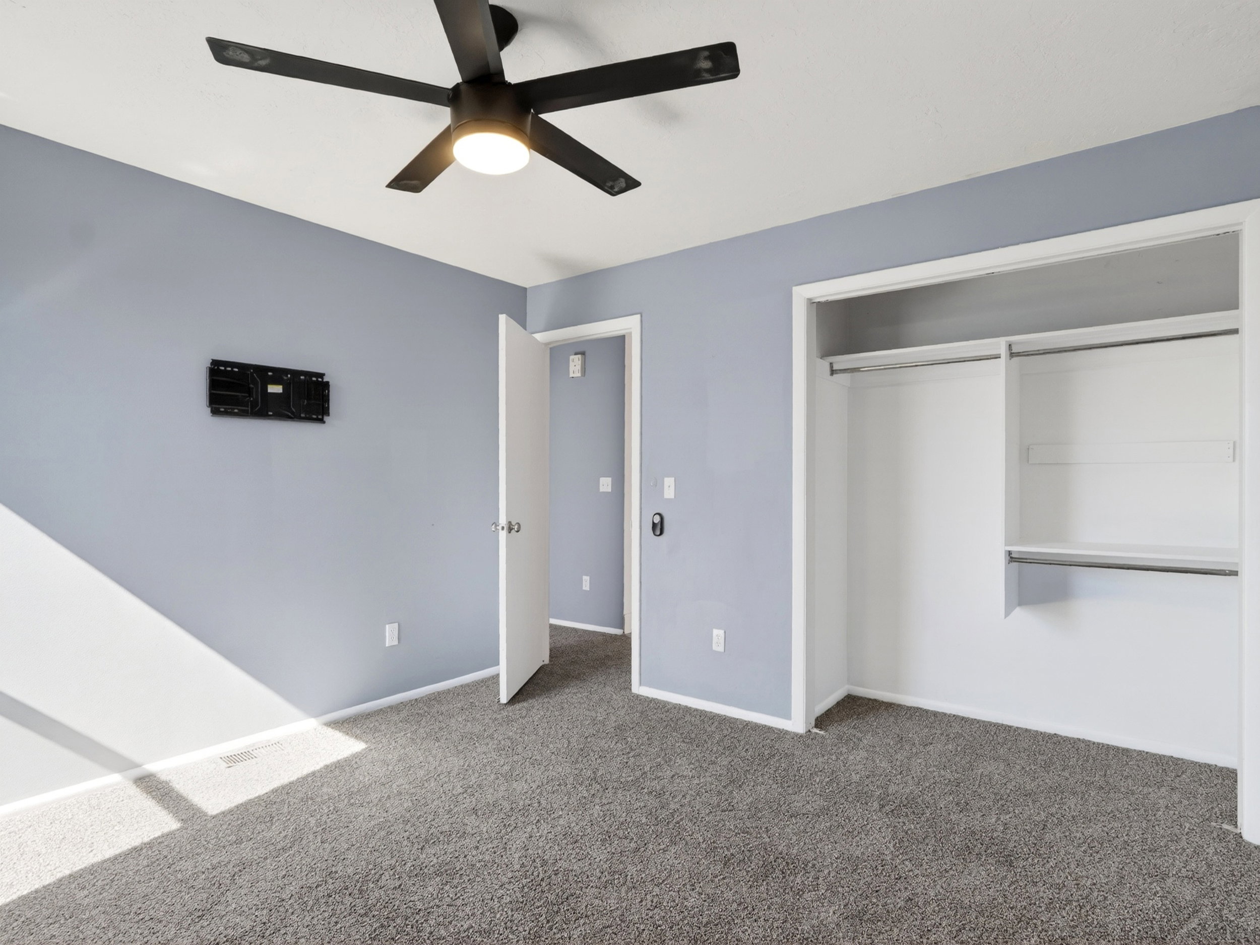 Bedroom featuring gray carpeting, light blue walls, and a black ceiling fan with integrated lighting