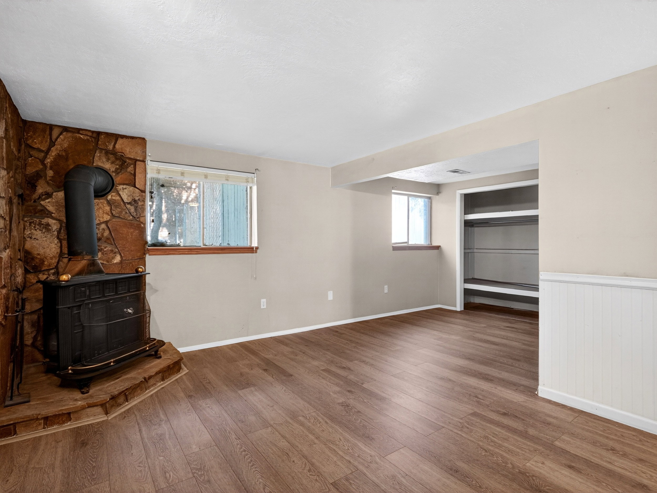 Spacious interior with wood-finish flooring, a stone accent wall, and a traditional wood-burning stove with a hearth
