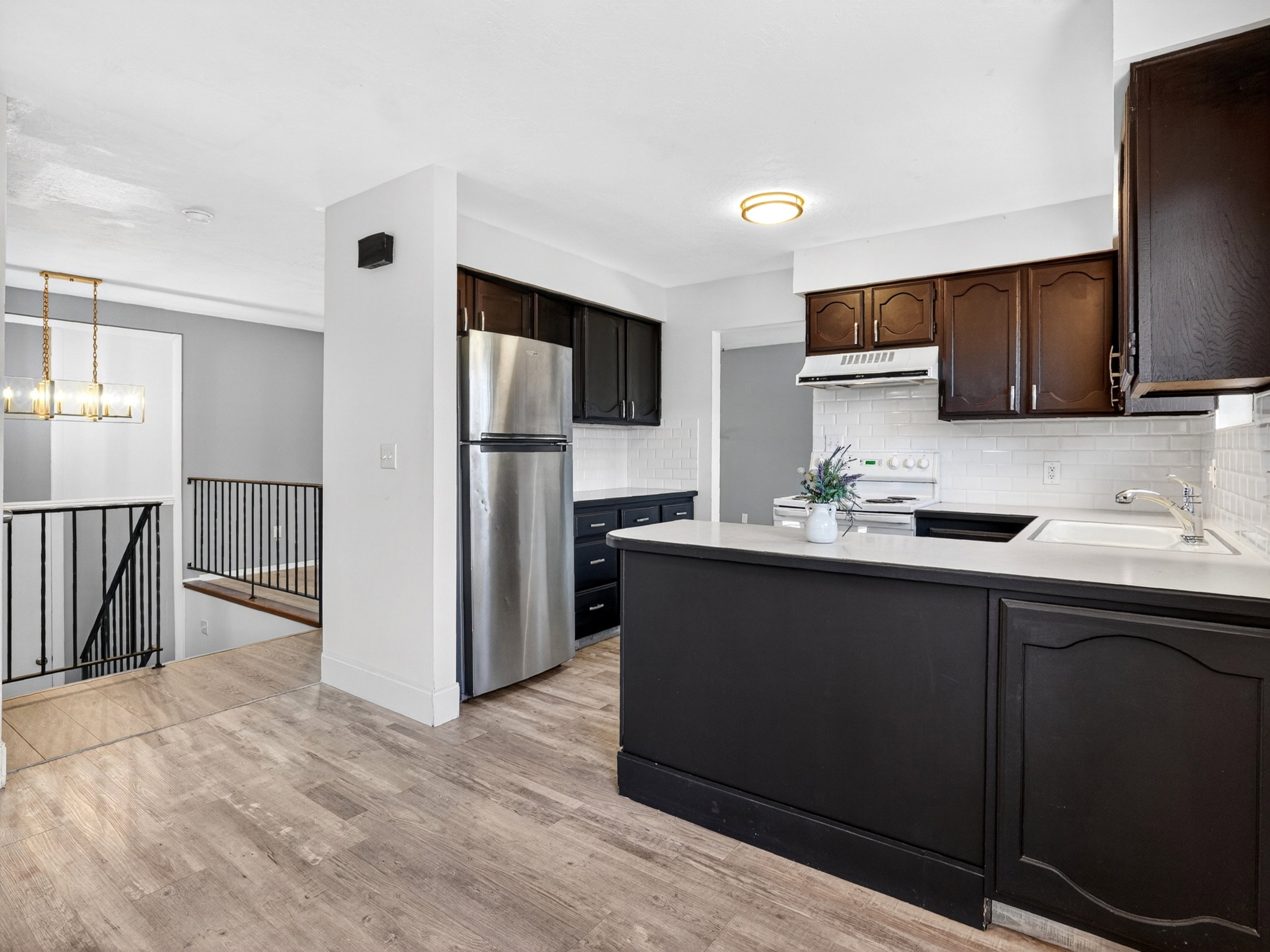 Contemporary kitchen featuring dark cabinetry, stainless steel refrigerator, white subway tile backsplash, and light-toned countertops