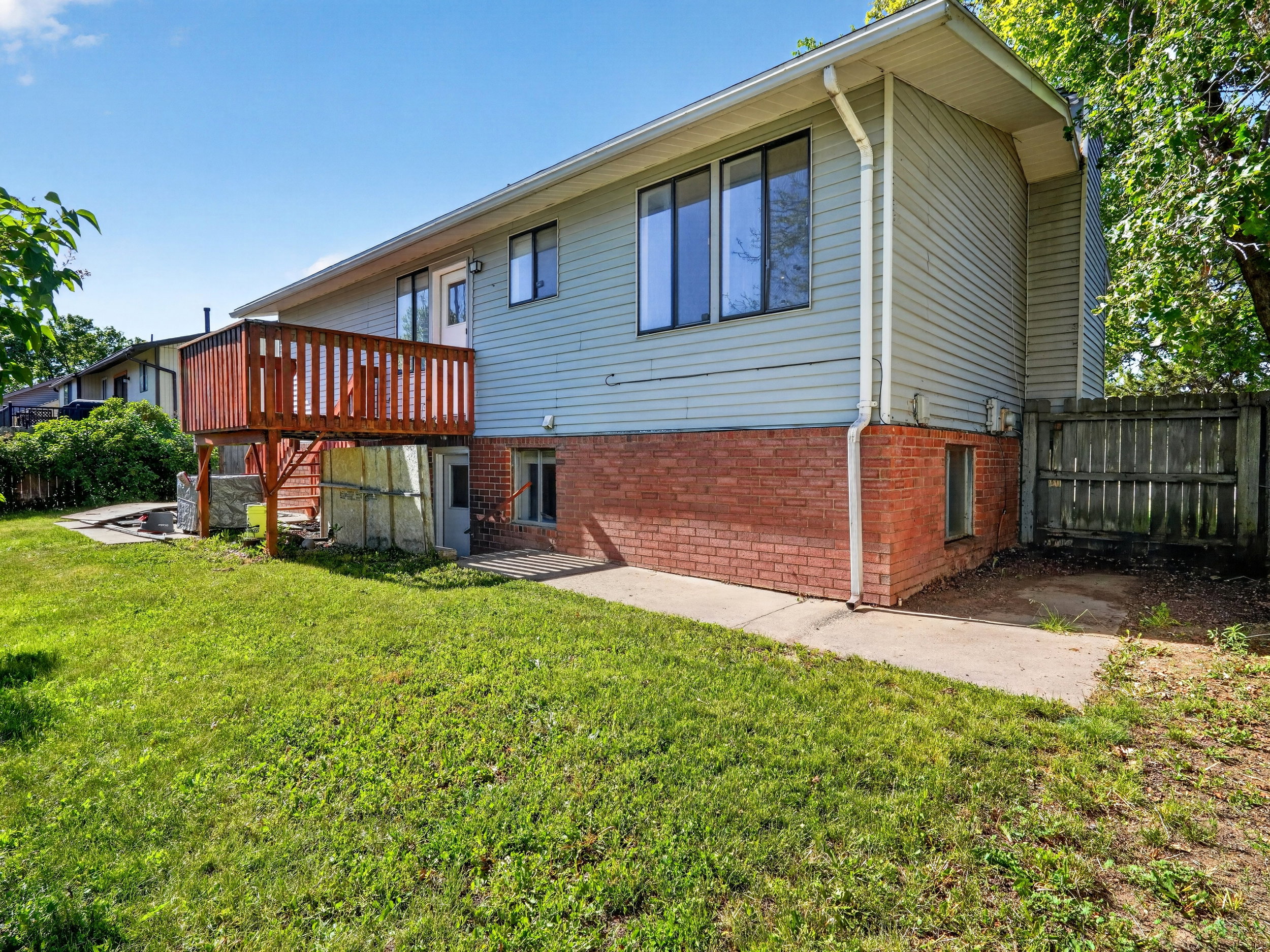 Rear exterior featuring a raised wooden deck, light-colored siding, and a brick base