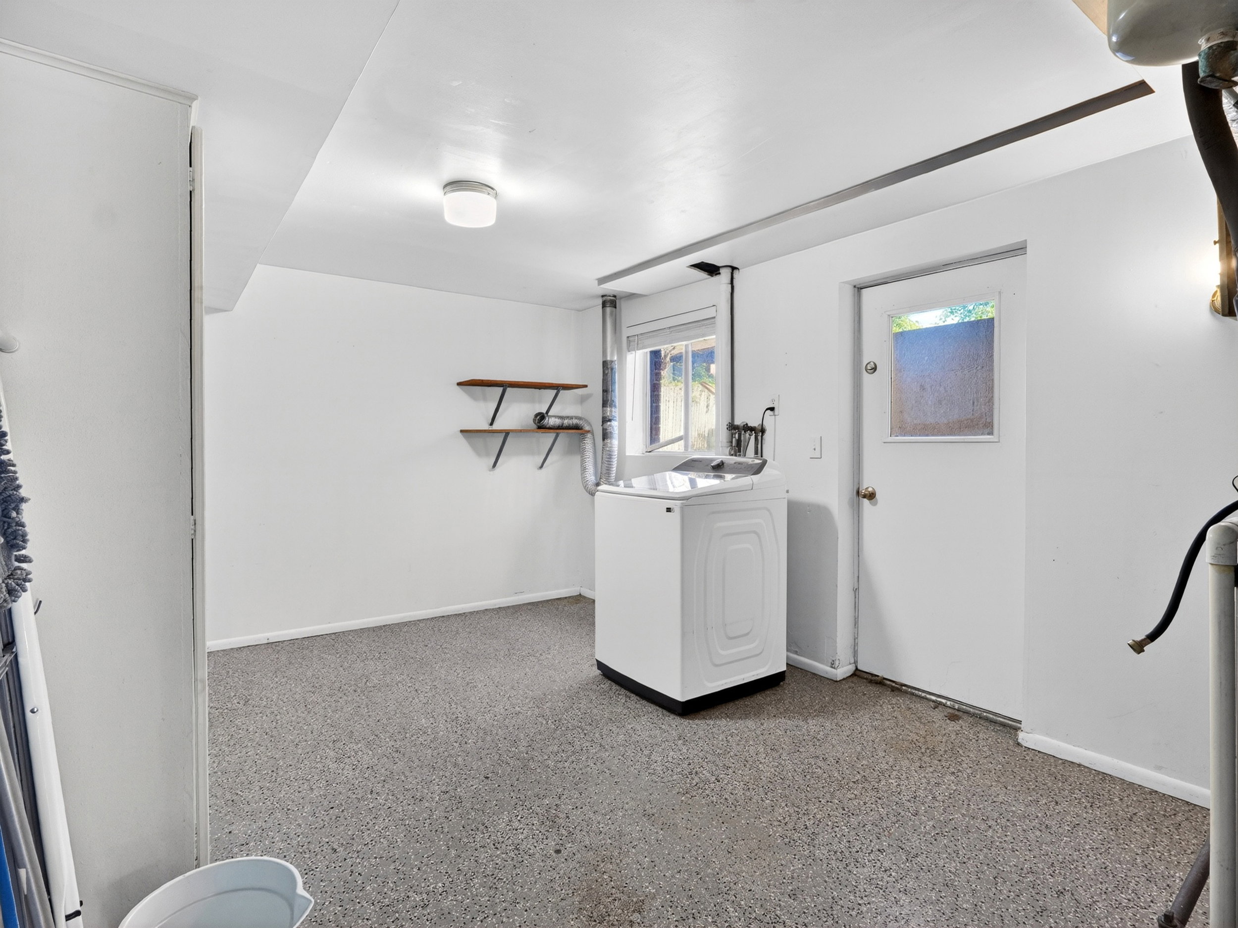 Utility area featuring durable speckled flooring, bright white walls, and a window for natural light
