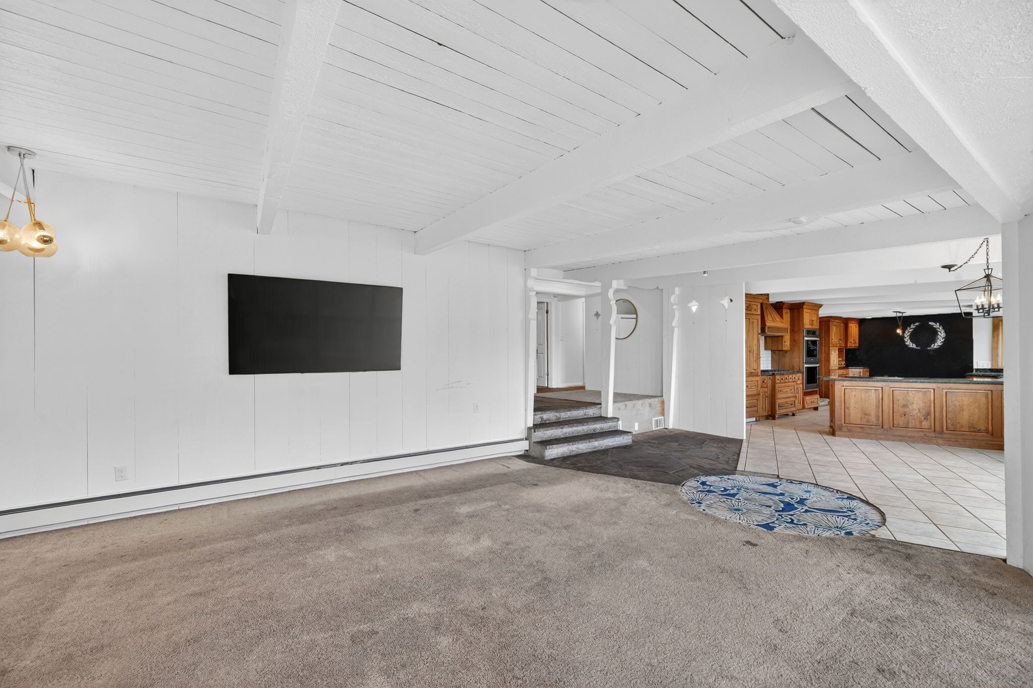 Open-concept living space featuring exposed white ceiling beams and neutral carpeting
