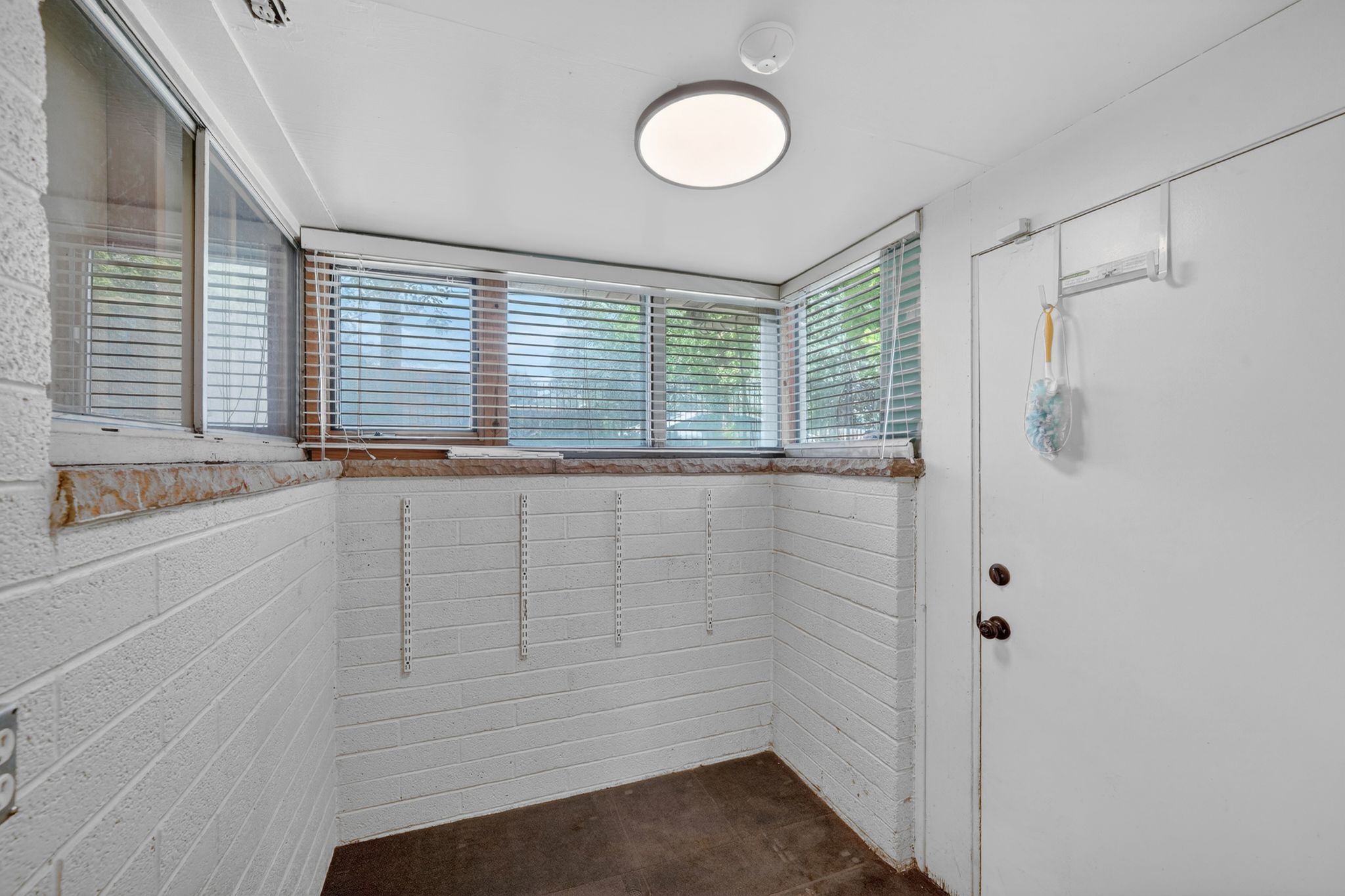 White painted brick walls with multiple windows, featuring blinds, and a solid door with dark hardware