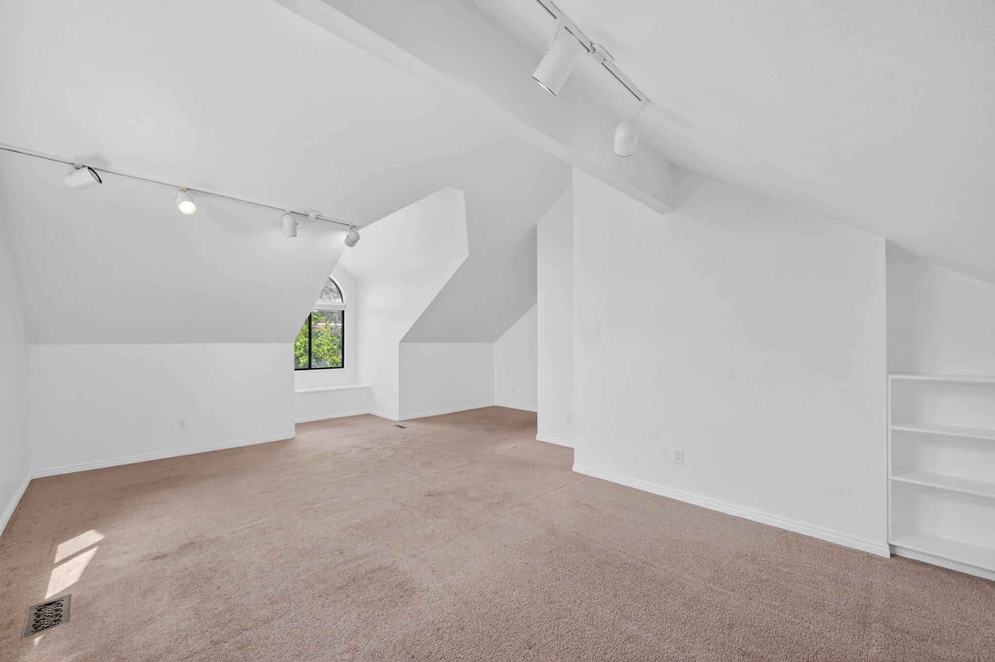 Spacious room featuring vaulted ceilings, track lighting, an arched window, and built-in shelving