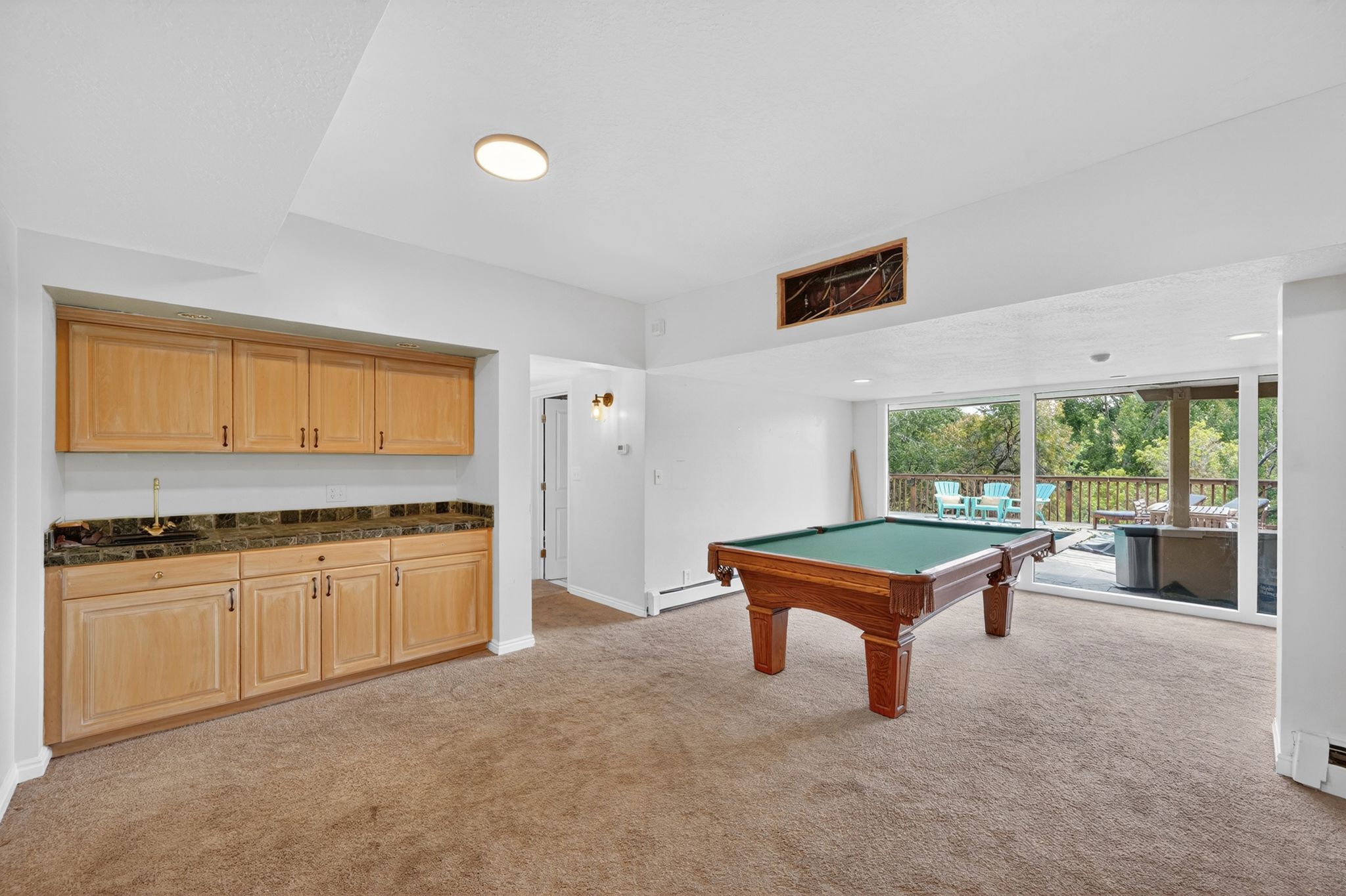 Lower-level entertainment space featuring a wet bar with light wood cabinetry, stone-finish countertop, and a brass faucet