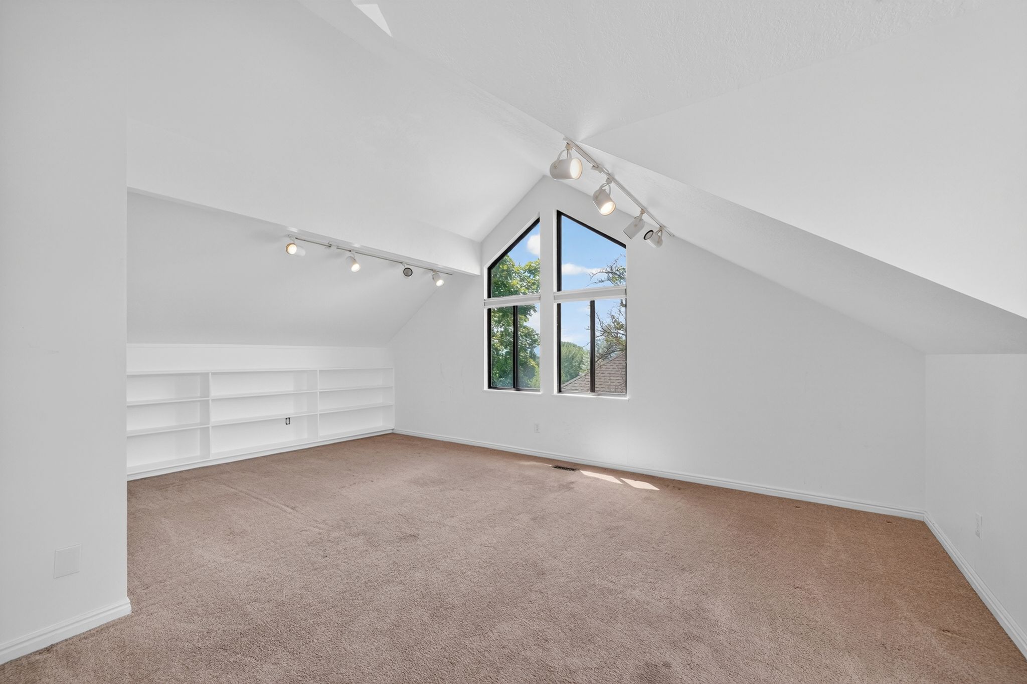 Spacious room featuring vaulted ceilings, track lighting, and a large multi-pane window