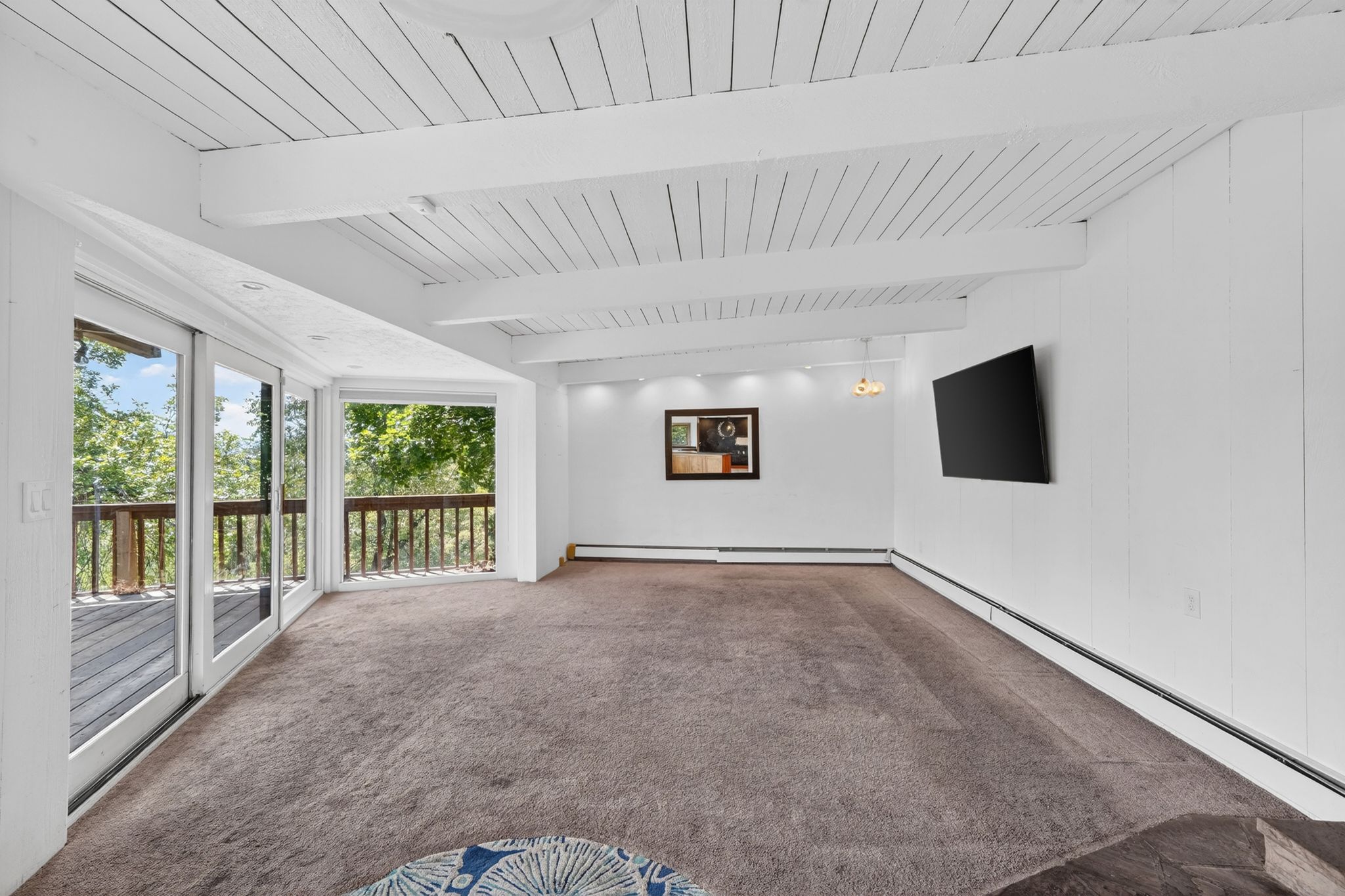 Bright living area featuring a wood-beam ceiling, plush carpet flooring, recessed lighting, and expansive sliding glass doors opening to an outdoor deck