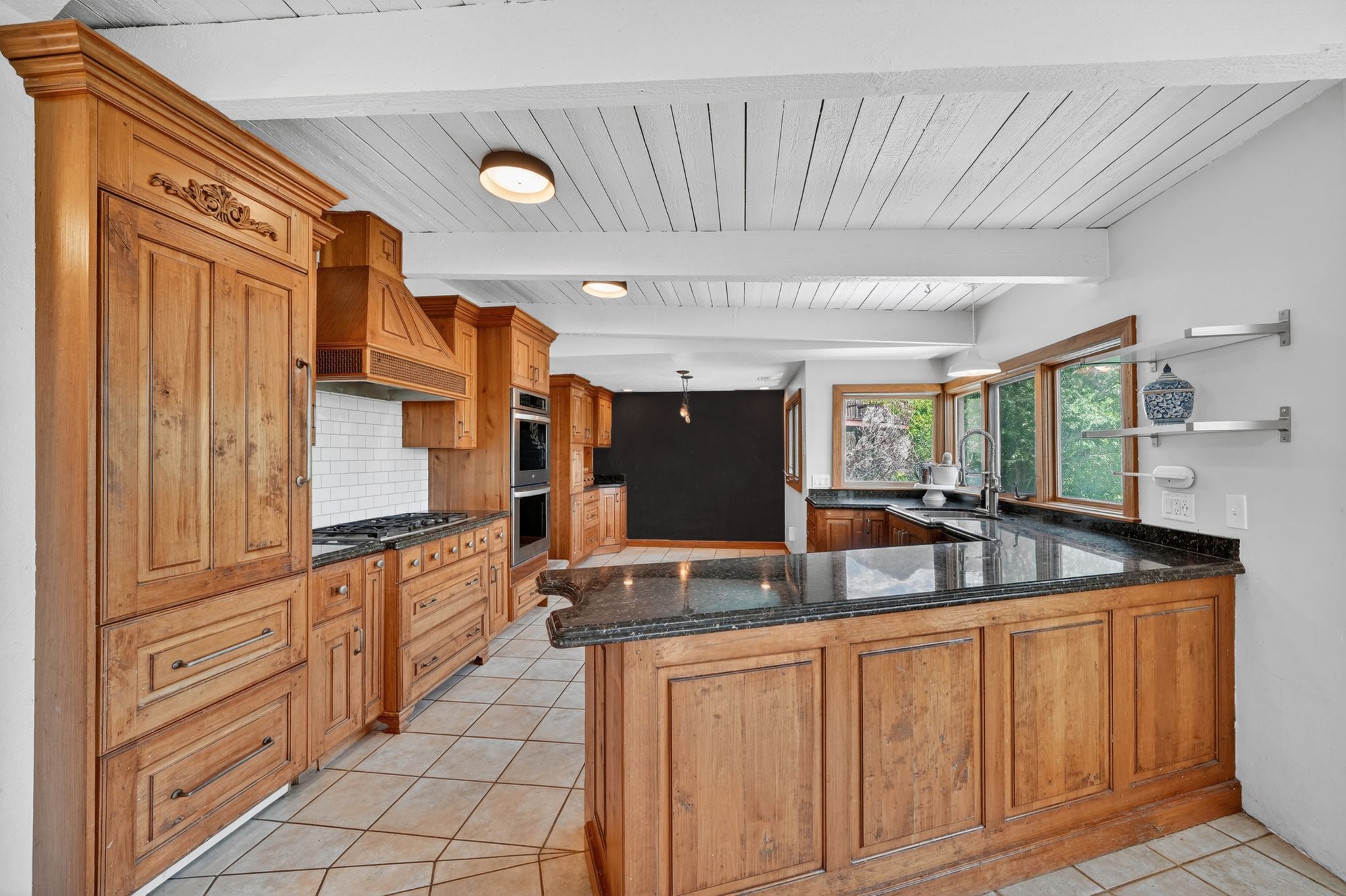 Kitchen featuring custom wood cabinetry, dark granite countertops, tile flooring, built-in appliances, and a wood plank ceiling