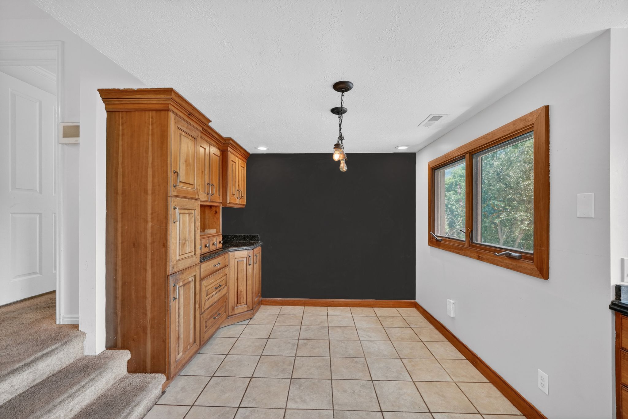 Built-in wood cabinetry with dark countertops, tile flooring, and a large window with wood trim
