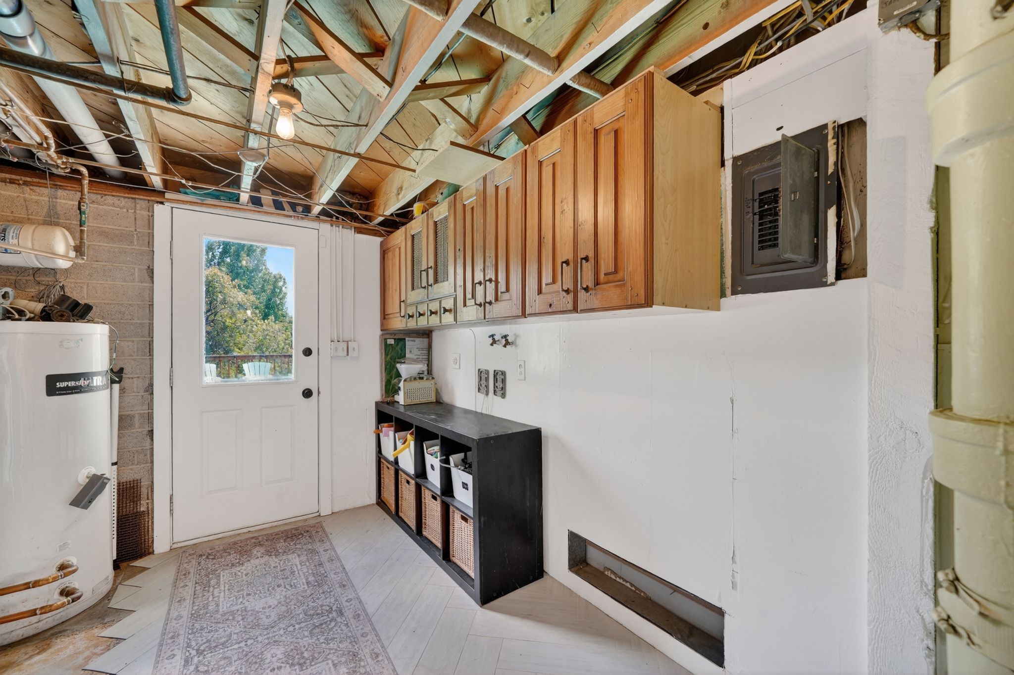 Utility space featuring light wood-finish flooring, exposed ceiling joists, and a glass-paneled exterior door