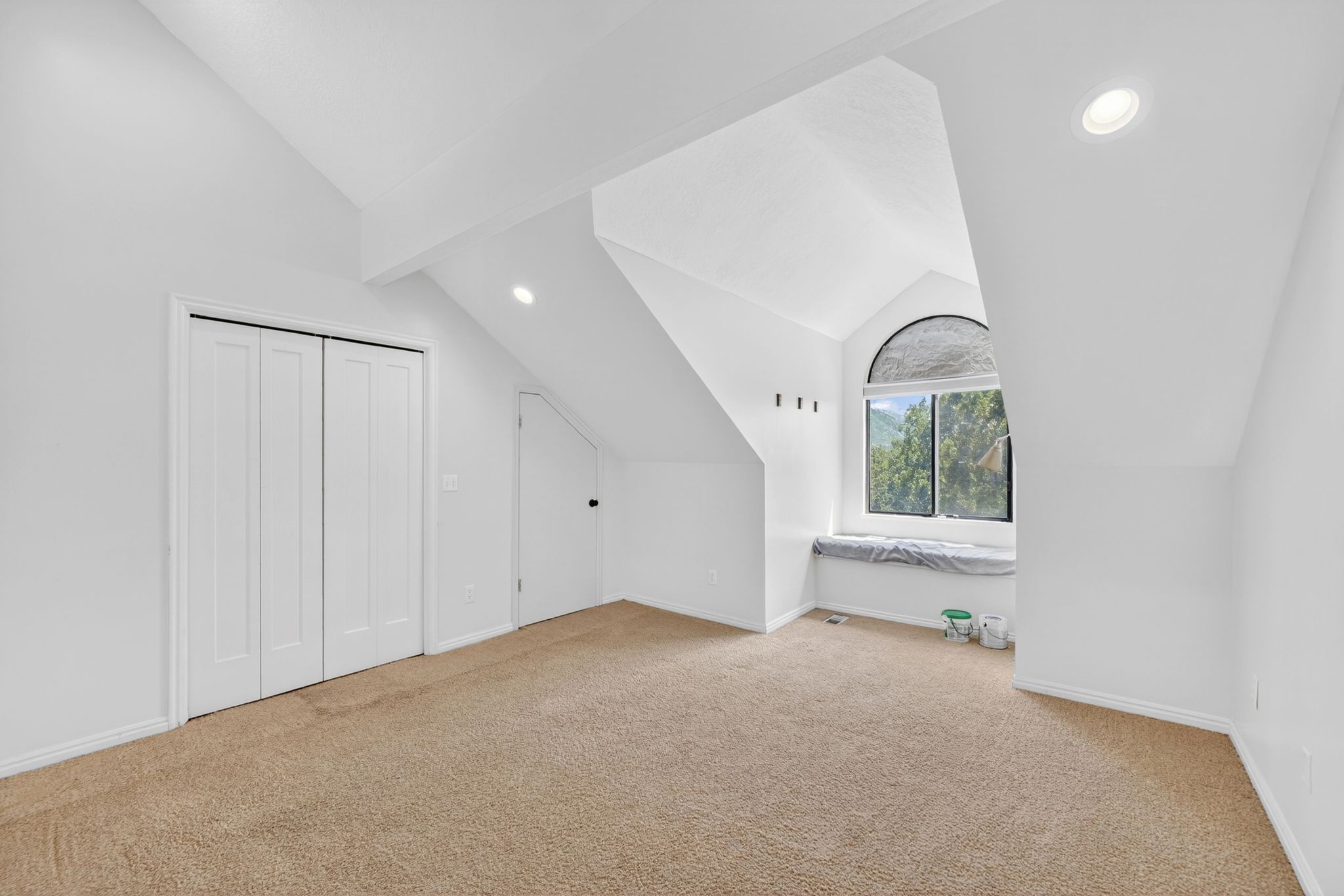 Carpeted room featuring an arched window, window seat, recessed lighting, and white bi-fold closet doors