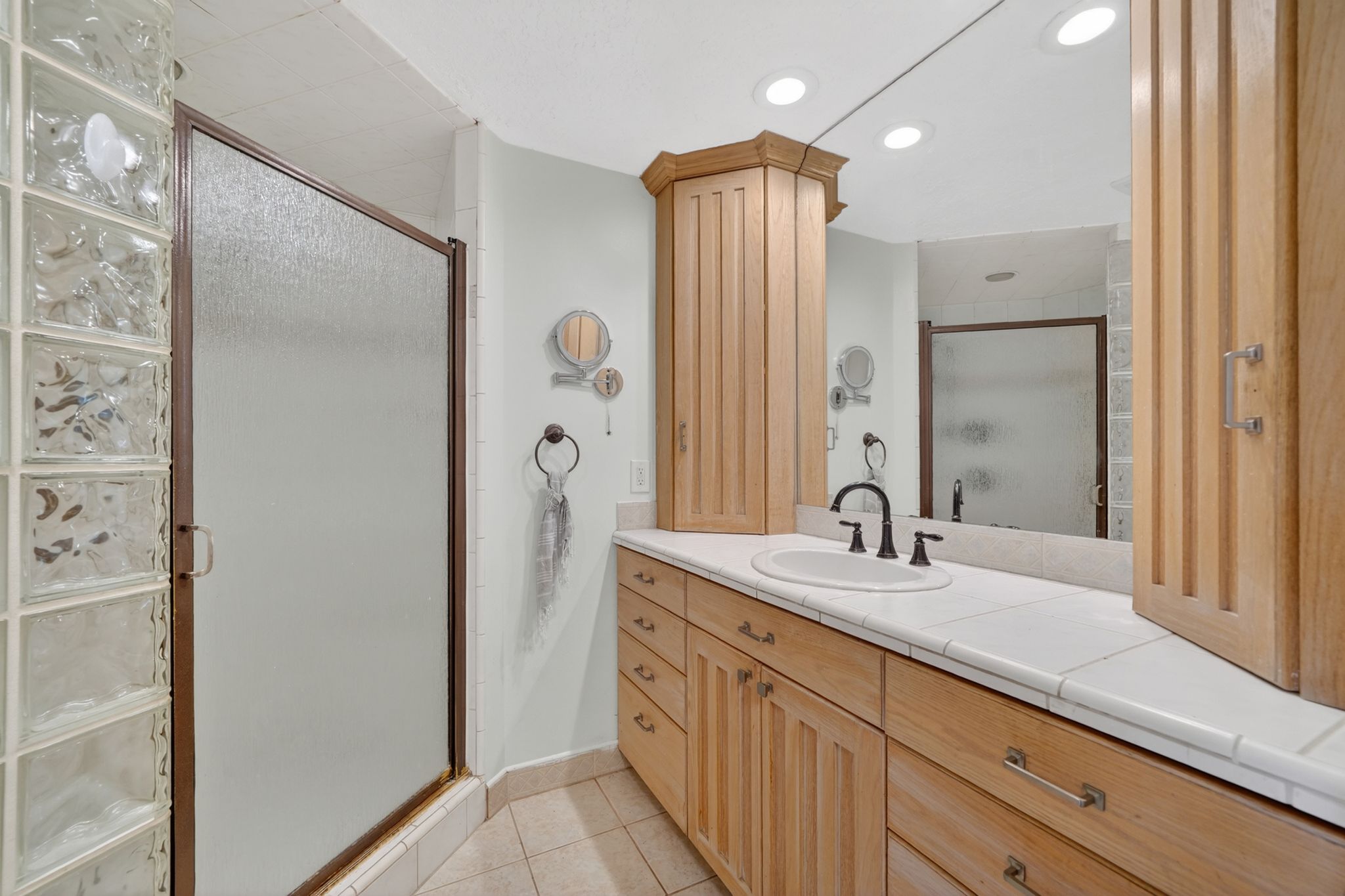 Bathroom vanity featuring light-toned wood cabinetry, a white tile countertop, and a built-in sink with a black faucet