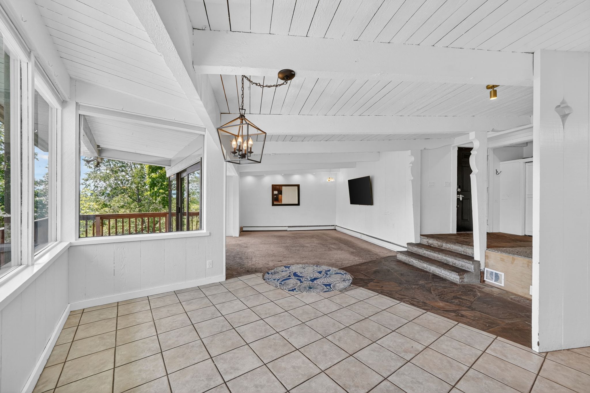 Spacious interior featuring a combination of tiled and carpeted flooring, exposed white ceiling beams, and a geometric chandelier