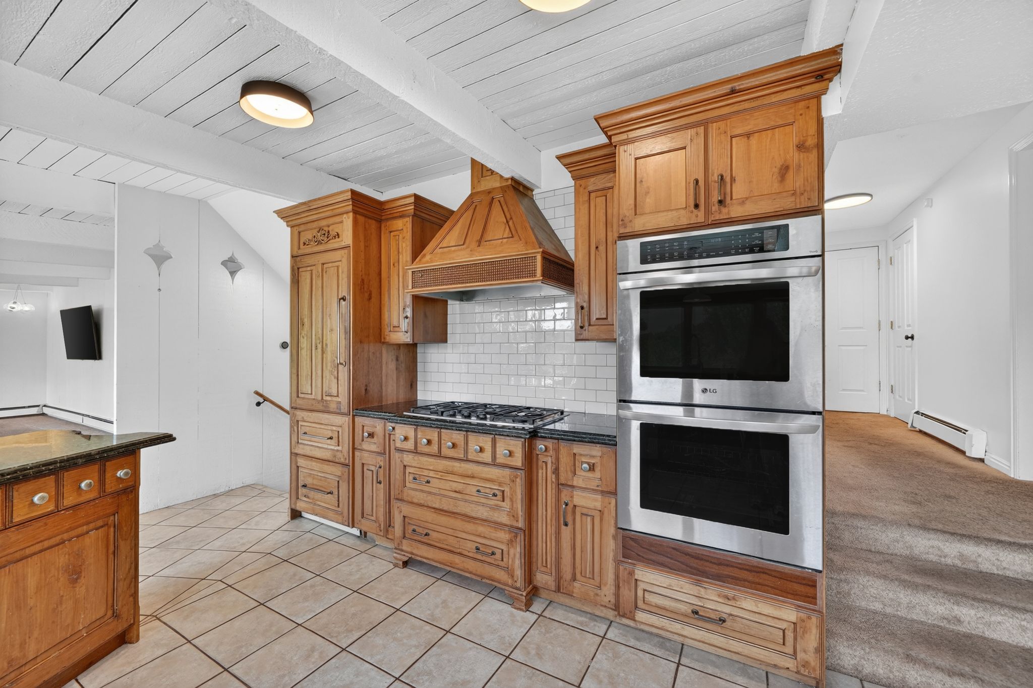 Kitchen featuring wood cabinetry, stainless steel double wall oven, gas cooktop, tile backsplash, and dark stone countertops