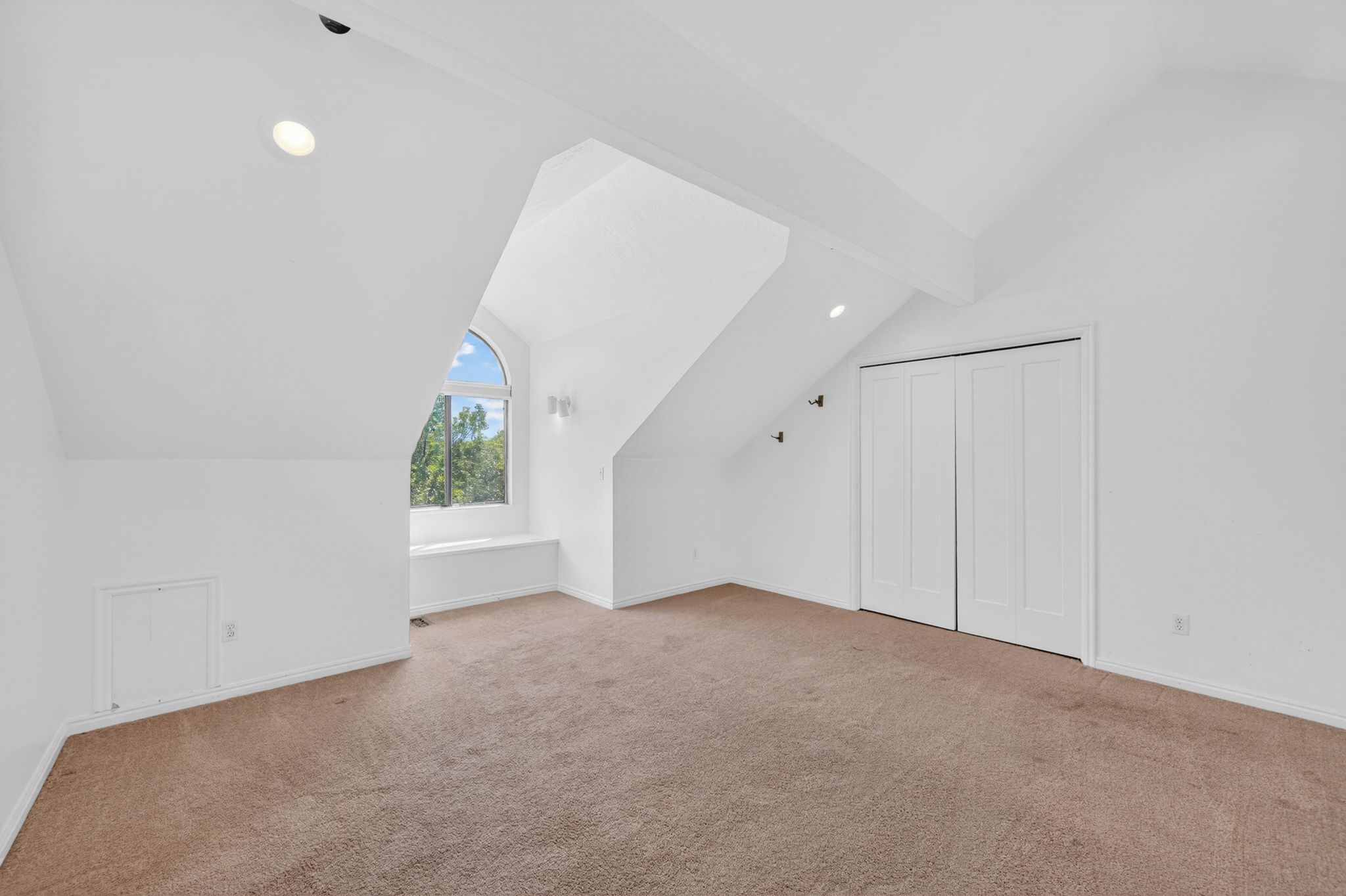 Attic space featuring an arched window with a window seat, sloped ceilings, recessed lighting, and a closet with bifold doors