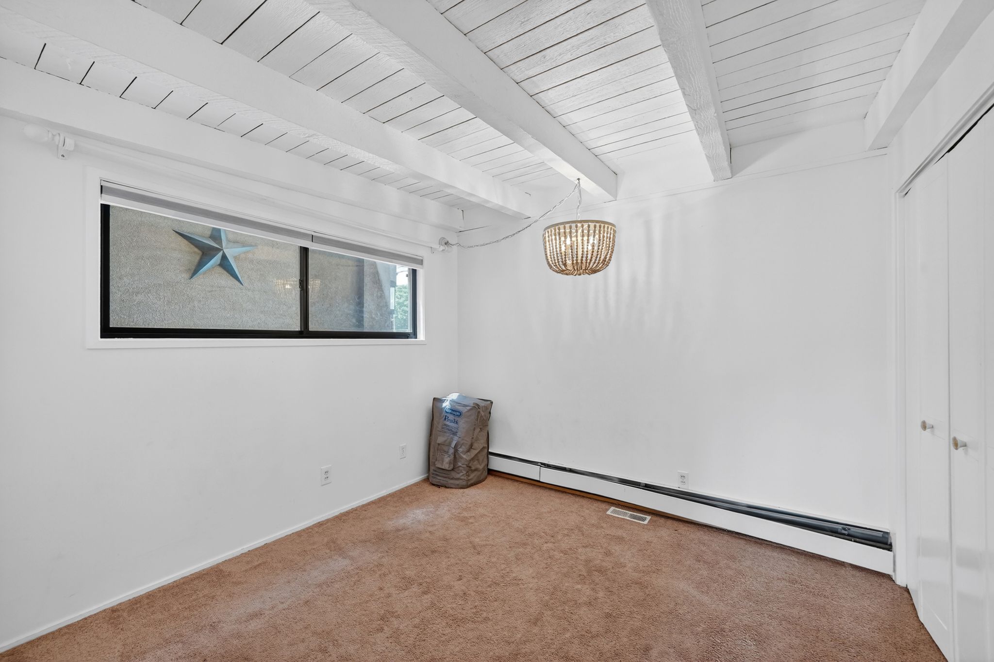 Room featuring exposed white-painted ceiling beams, a decorative suspended light fixture, and a horizontal window with black trim