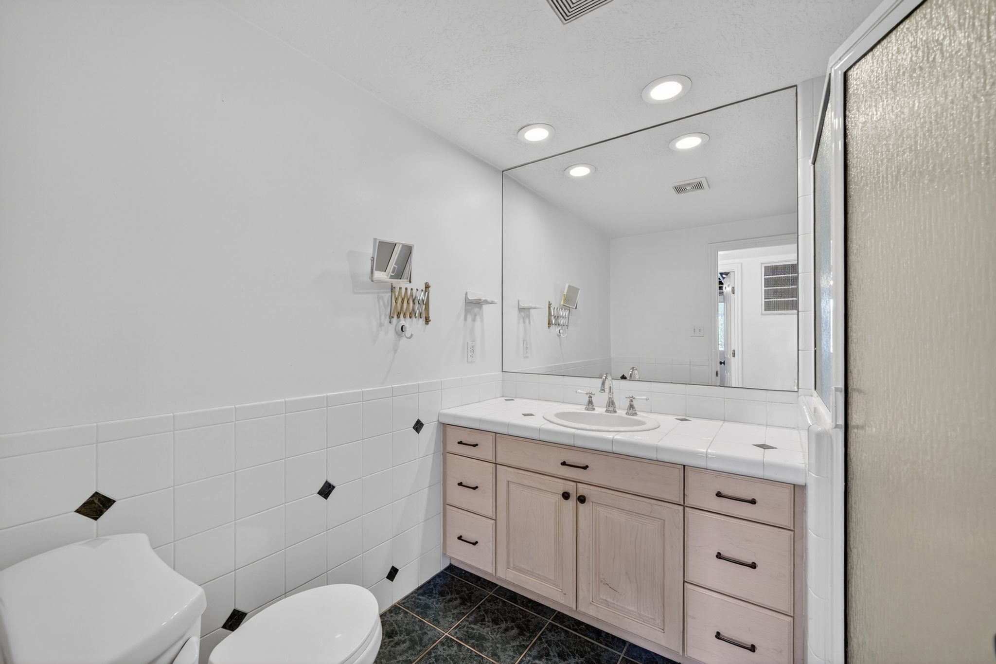 Bathroom featuring a spacious vanity with integrated sink, a large mirror, recessed ceiling lighting, a tiled countertop, and wood-finish cabinetry with dark hardware