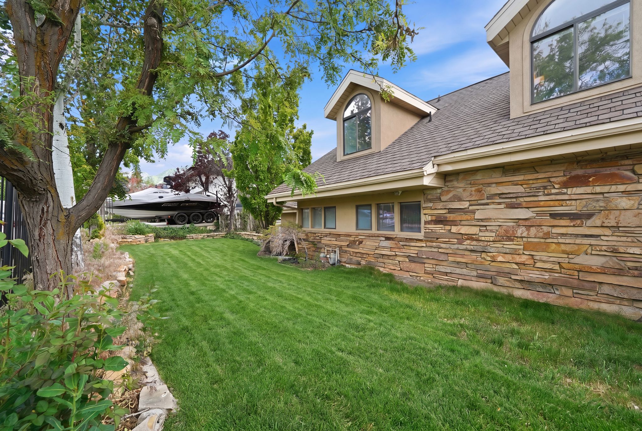 Expansive side yard featuring a manicured lawn, established trees, and natural stone retaining walls