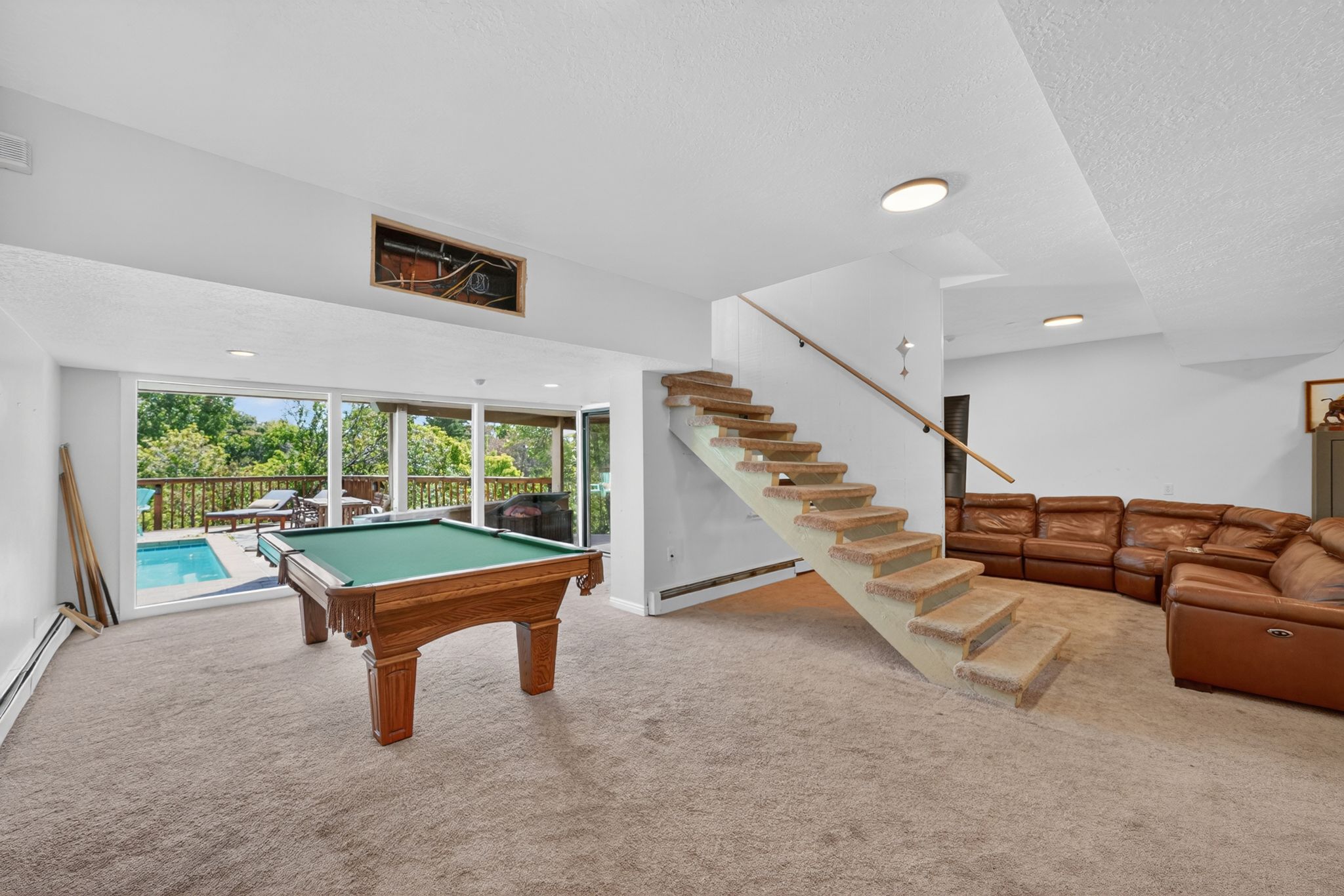 Spacious lower level featuring a carpeted floor, recessed lighting, and a prominent staircase with a wood handrail