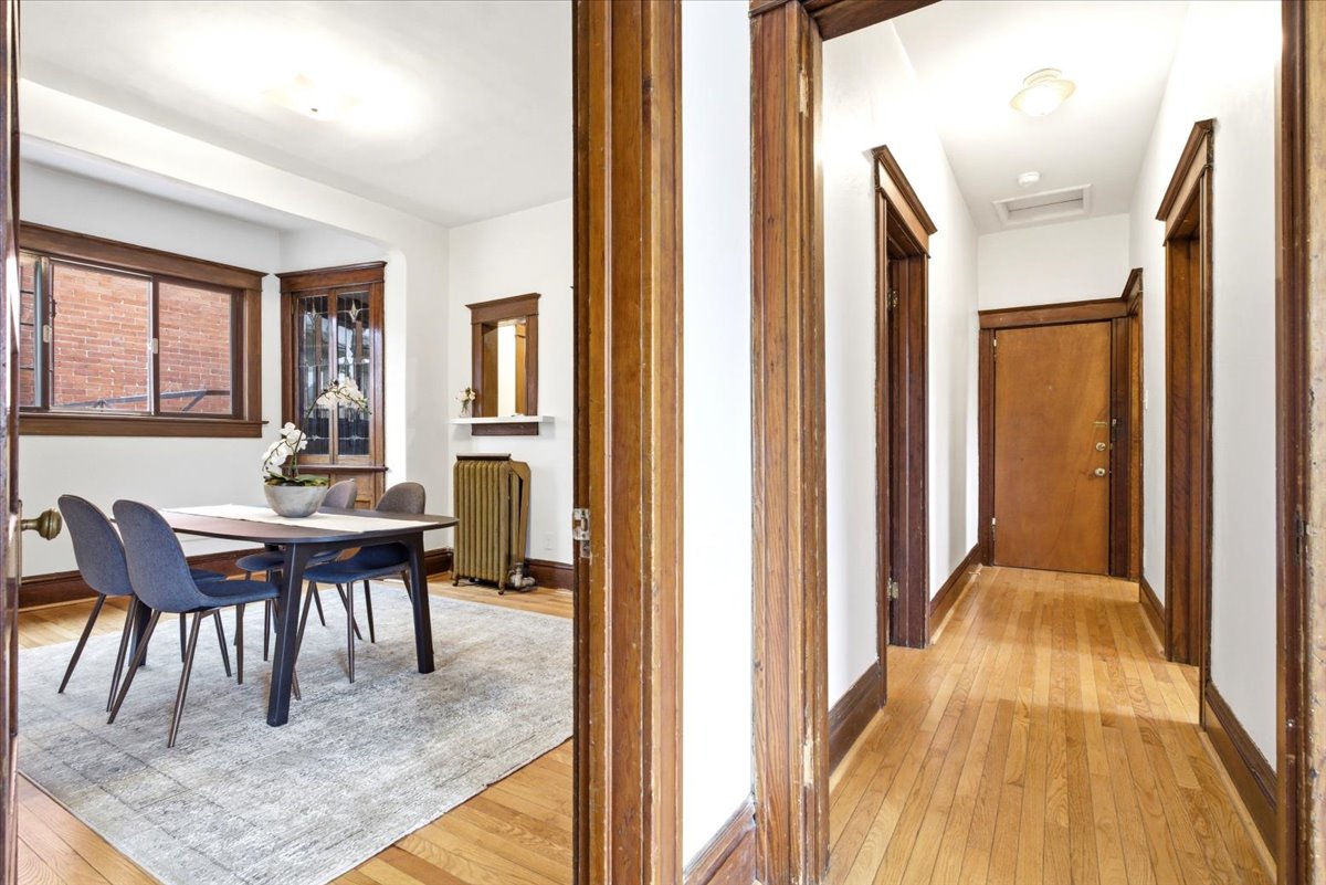 Hardwood flooring extends throughout the hallway and into a room featuring a bay window, wood trim, and a built-in corner cabinet with leaded glass
