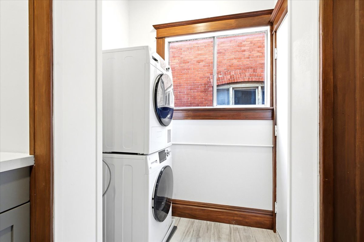 Dedicated laundry area with stackable appliances, wood-finish trim, and light wood-look flooring