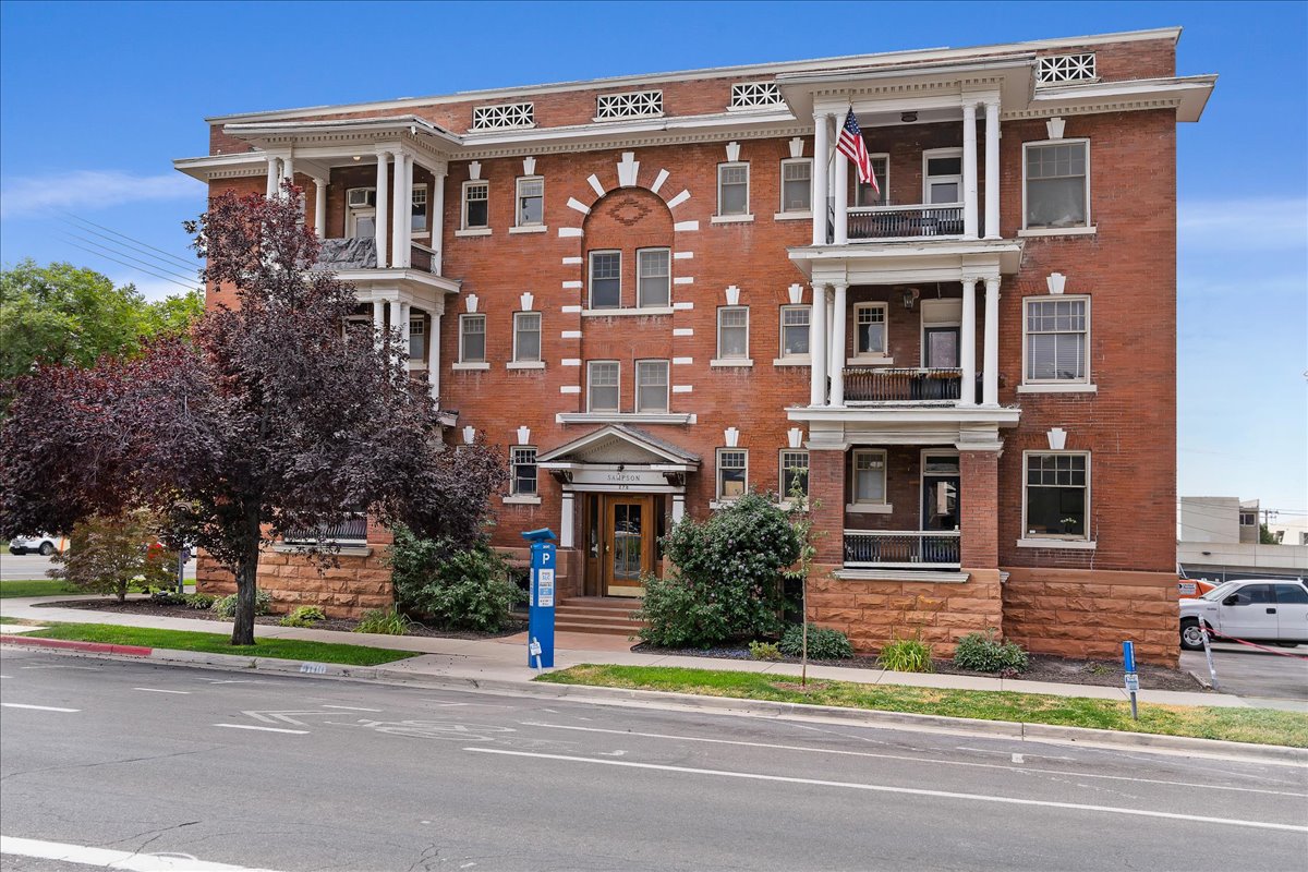 Brick exterior building featuring multiple balconies, decorative white trim, arched entryway, and stone foundation