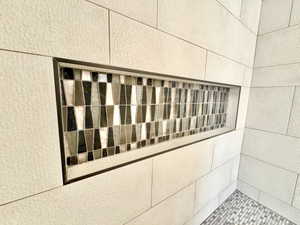 Built-in shower niche featuring mosaic tile inlay, surrounded by large format textured wall tiles and coordinated mosaic floor tiles
