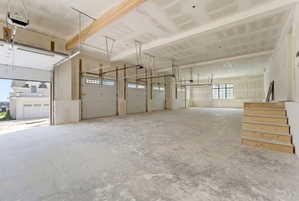 Spacious garage featuring a concrete floor, four overhead doors, exposed wood beams, and multiple windows providing natural light