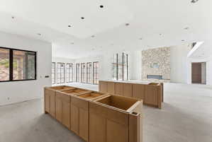 Spacious open-concept interior featuring light wood-finish cabinetry, a stone accent wall with a built-in fireplace, recessed ceiling lighting, and multiple black-framed windows providing abundant natural light