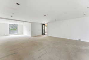 Spacious interior room featuring white walls, recessed ceiling lighting, a large multi-pane window, and an exterior glass door