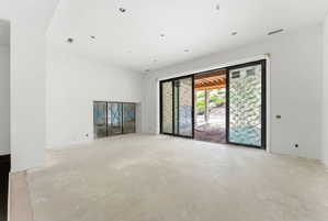 Spacious unfinished interior featuring a large sliding glass door, recessed lighting, and a built-in alcove with glass doors