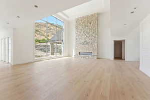 Expansive room featuring a floor-to-ceiling stone fireplace with a linear insert, wide plank wood-finish flooring, and a dramatic two-story window