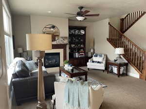 Living area featuring a fireplace with a tile surround and wood mantel, a built-in wood bookcase, a ceiling fan with light fixture, and a wood staircase with balusters