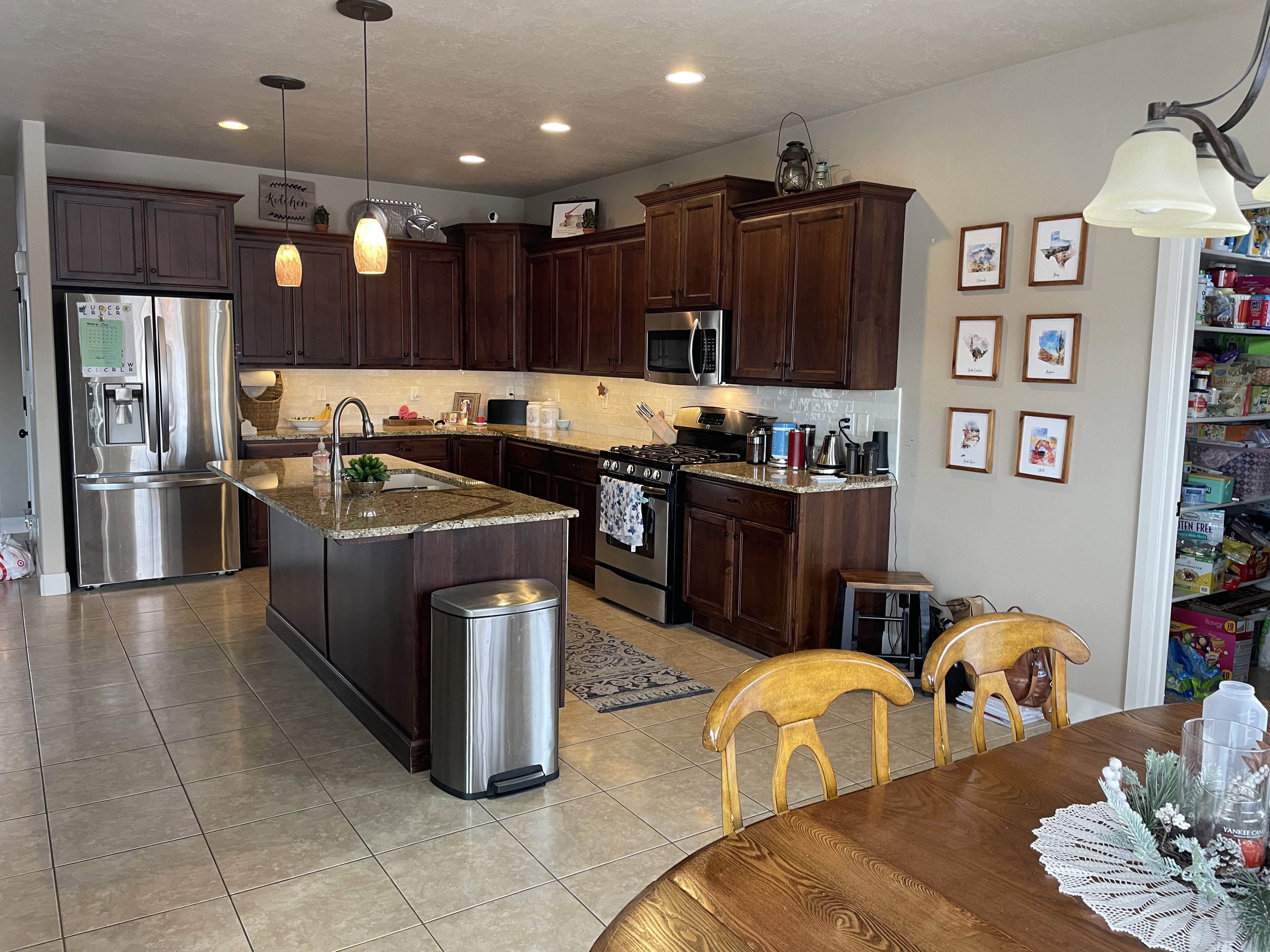 Kitchen featuring a large central island with an undermount sink, granite-style countertops, dark wood cabinetry, stainless steel appliances, and tile flooring