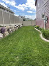 Expansive green lawn area featuring a decorative rock border with plantings, perimeter fencing, and a side access gate