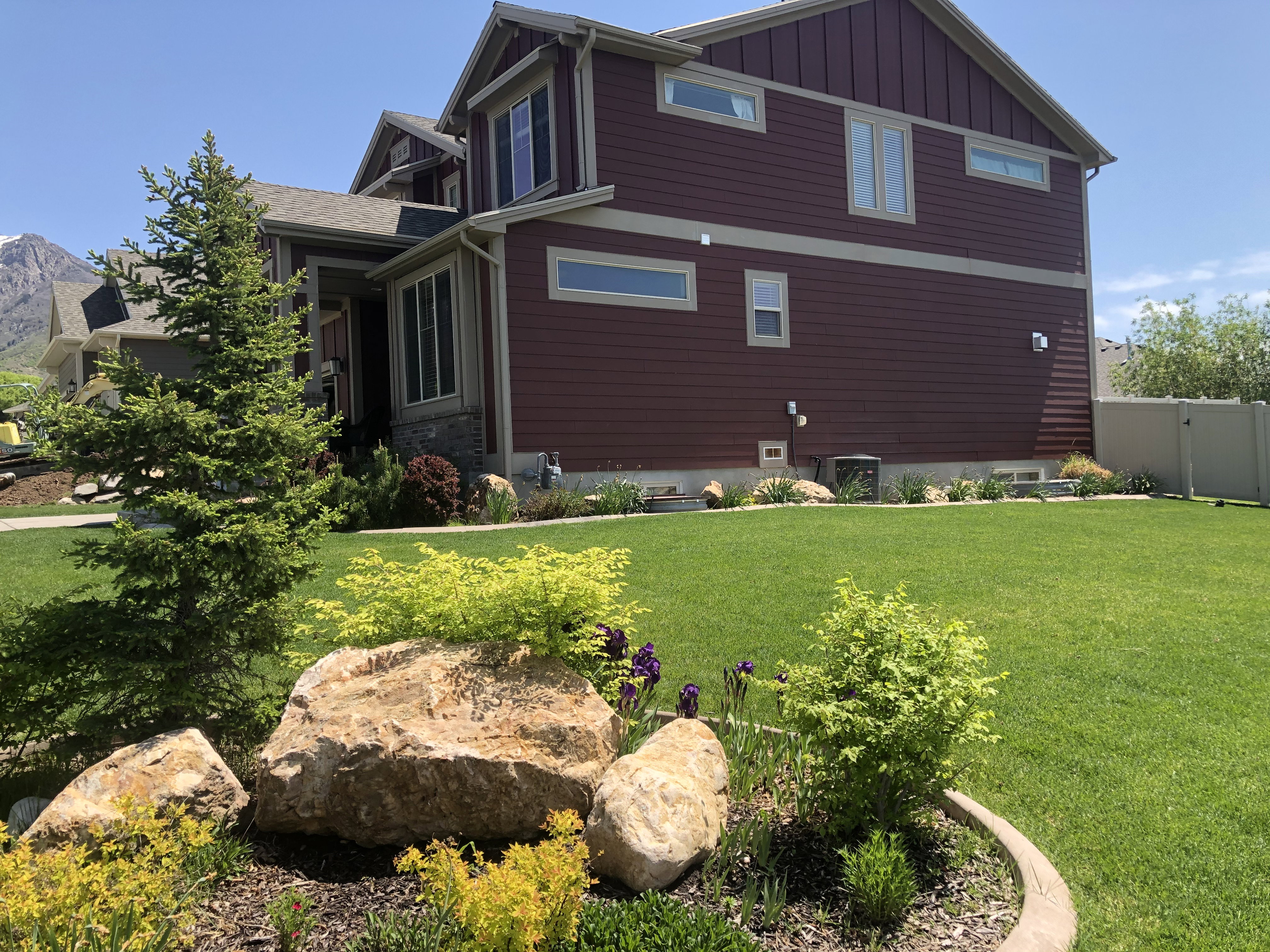 Spacious lawn featuring mature landscaping, decorative boulders, and planted garden beds