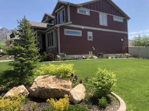 Spacious lawn featuring mature landscaping, decorative boulders, and planted garden beds