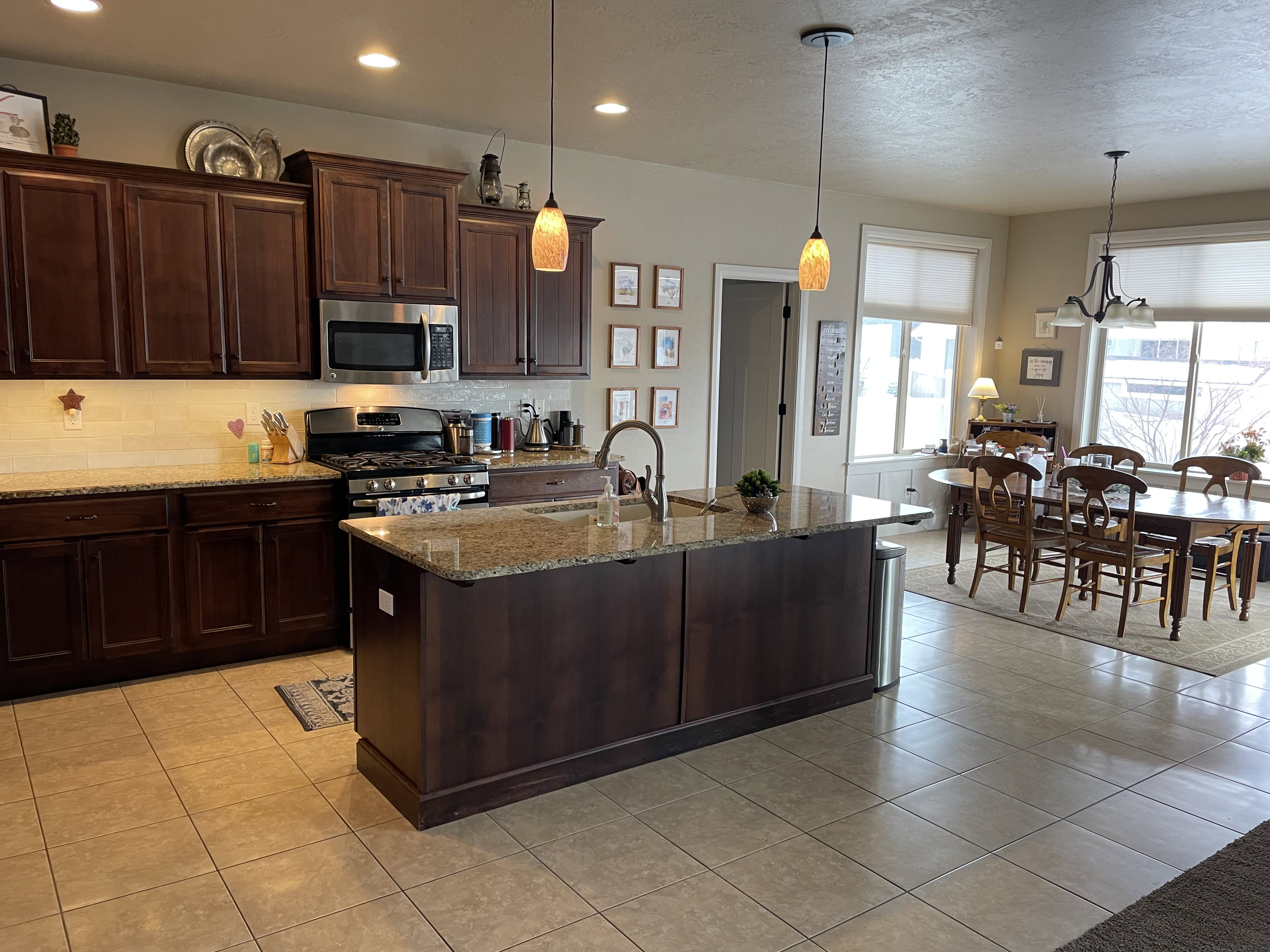 Kitchen featuring wood-finish cabinetry, granite countertops, tile flooring, stainless steel appliances, and a central island with pendant lighting