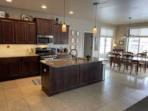 Kitchen featuring wood-finish cabinetry, granite countertops, tile flooring, stainless steel appliances, and a central island with pendant lighting