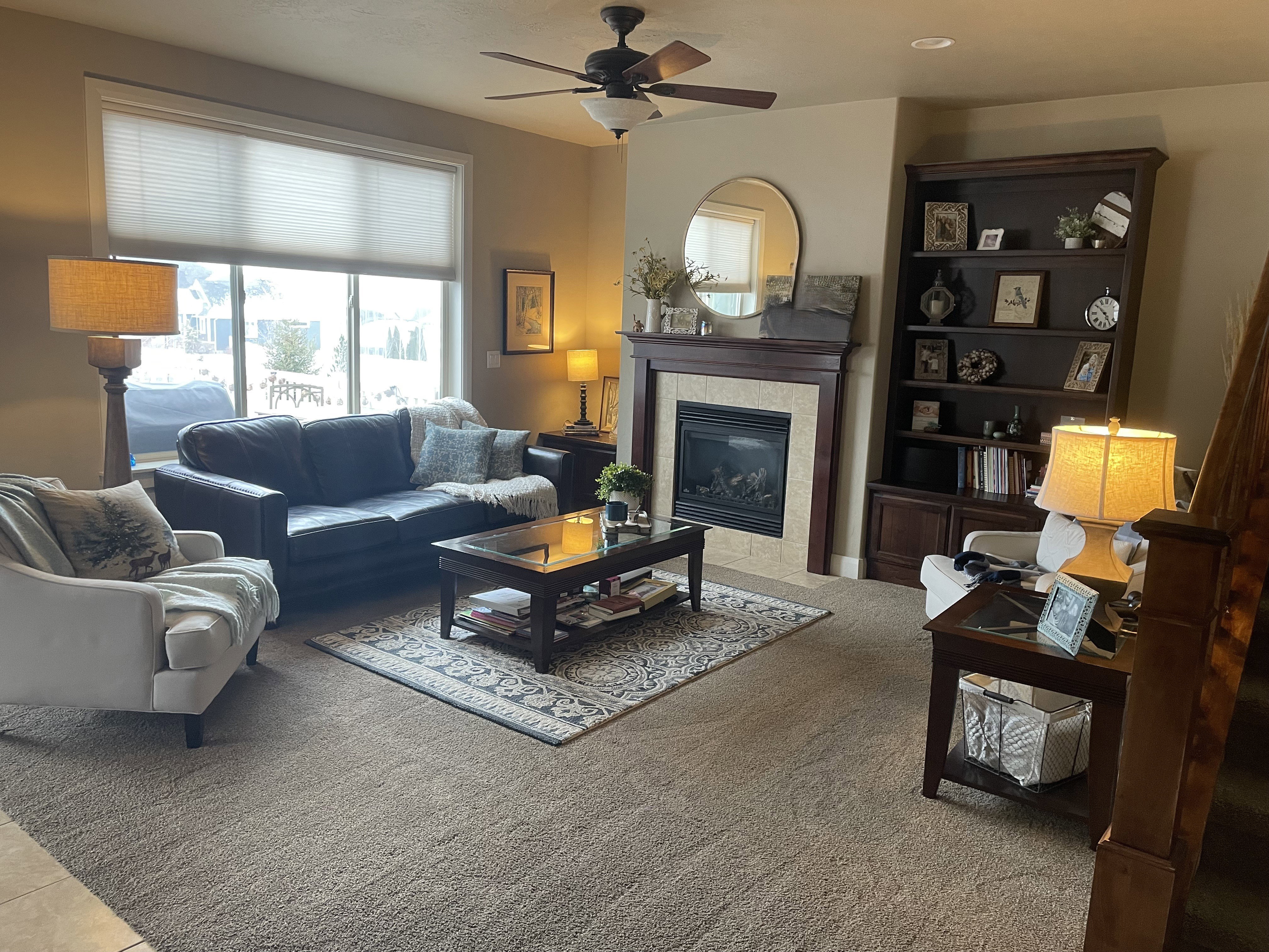 Spacious living area featuring a fireplace with a stone surround and wood mantle, a large window, recessed lighting, and a ceiling fan