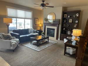 Spacious living area featuring a fireplace with a stone surround and wood mantle, a large window, recessed lighting, and a ceiling fan