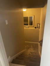 Carpeted staircase featuring a wooden handrail, neutral wall paint, and a wall-mounted light fixture