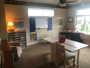 Carpeted room with a ceiling fan, featuring a large window with blinds, light tan wall color, and white baseboards