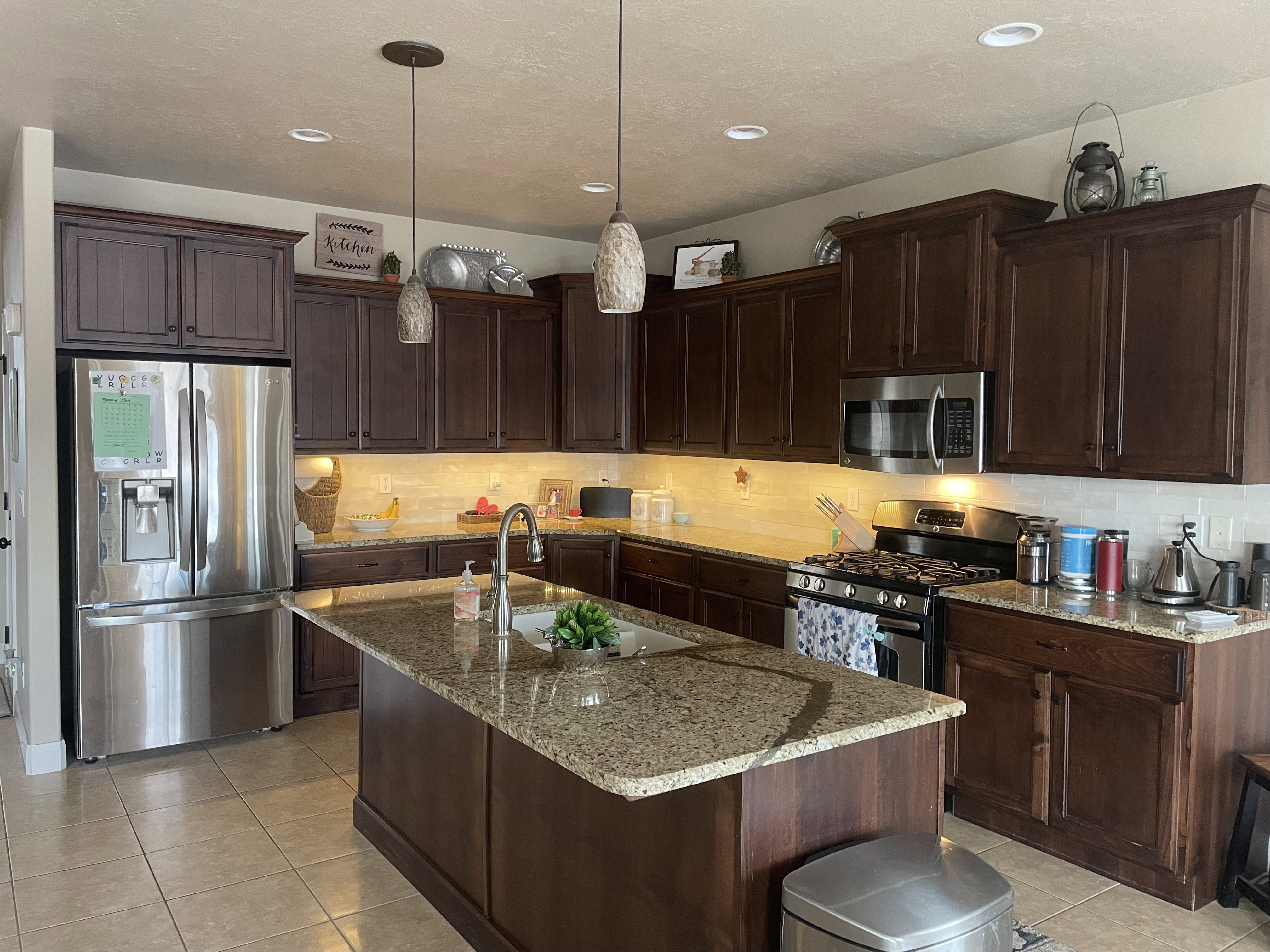 Kitchen featuring a central island with a sink, granite-style countertops, dark wood-finish cabinetry, stainless steel appliances, and recessed lighting