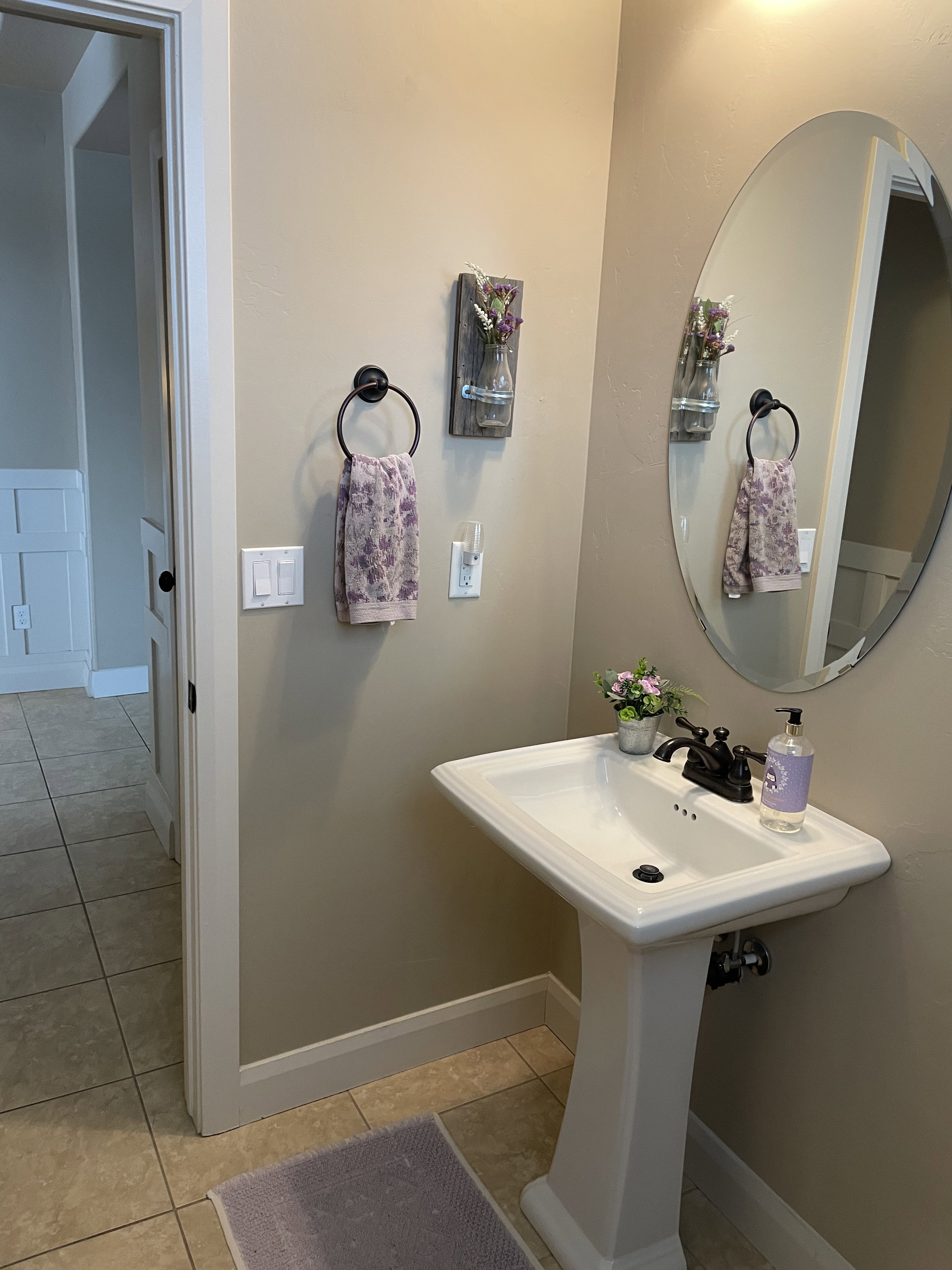 Pedestal sink with dark bronze faucet, oval mirror, and tile flooring