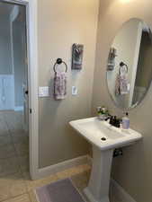 Pedestal sink with dark bronze faucet, oval mirror, and tile flooring